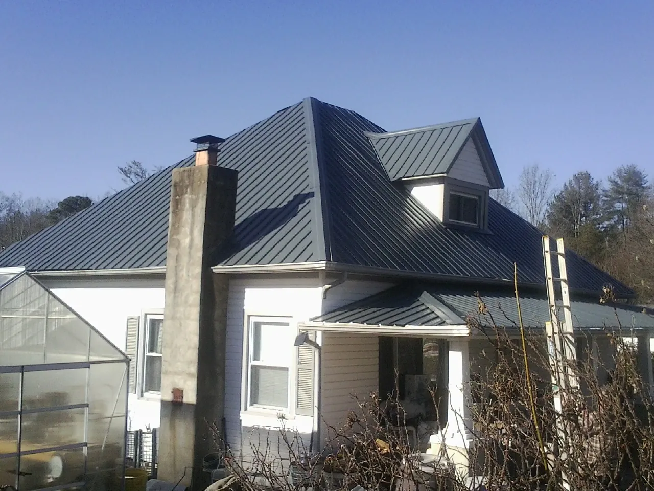 Dark blue standing seam metal roof on a white farmhouse with dormer — Slate & Tile Roof Repair by Roofing Brothers in Nebo