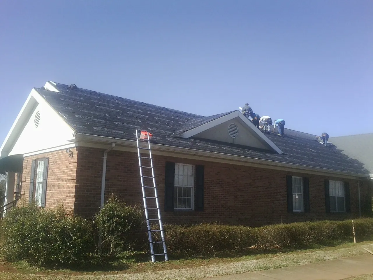 Crew tearing shingles off a brick ranch roof with a ladder set — Metal Roof Repair work by our crew in Nebo