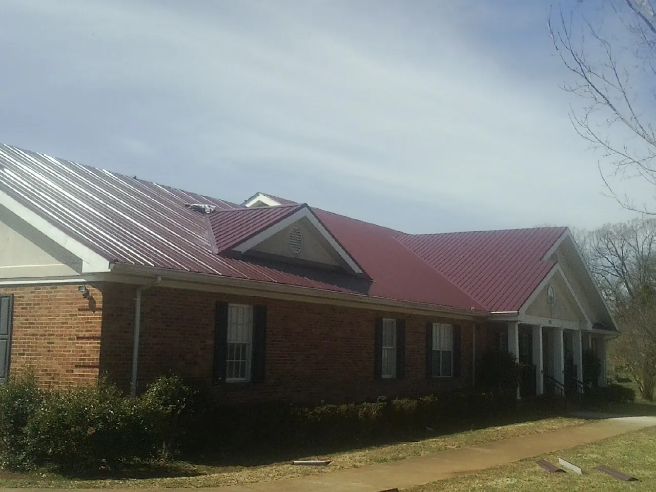 Red metal roof with gabled entries on a long brick building, from a Hail Damage Roof Repair job in Nebo