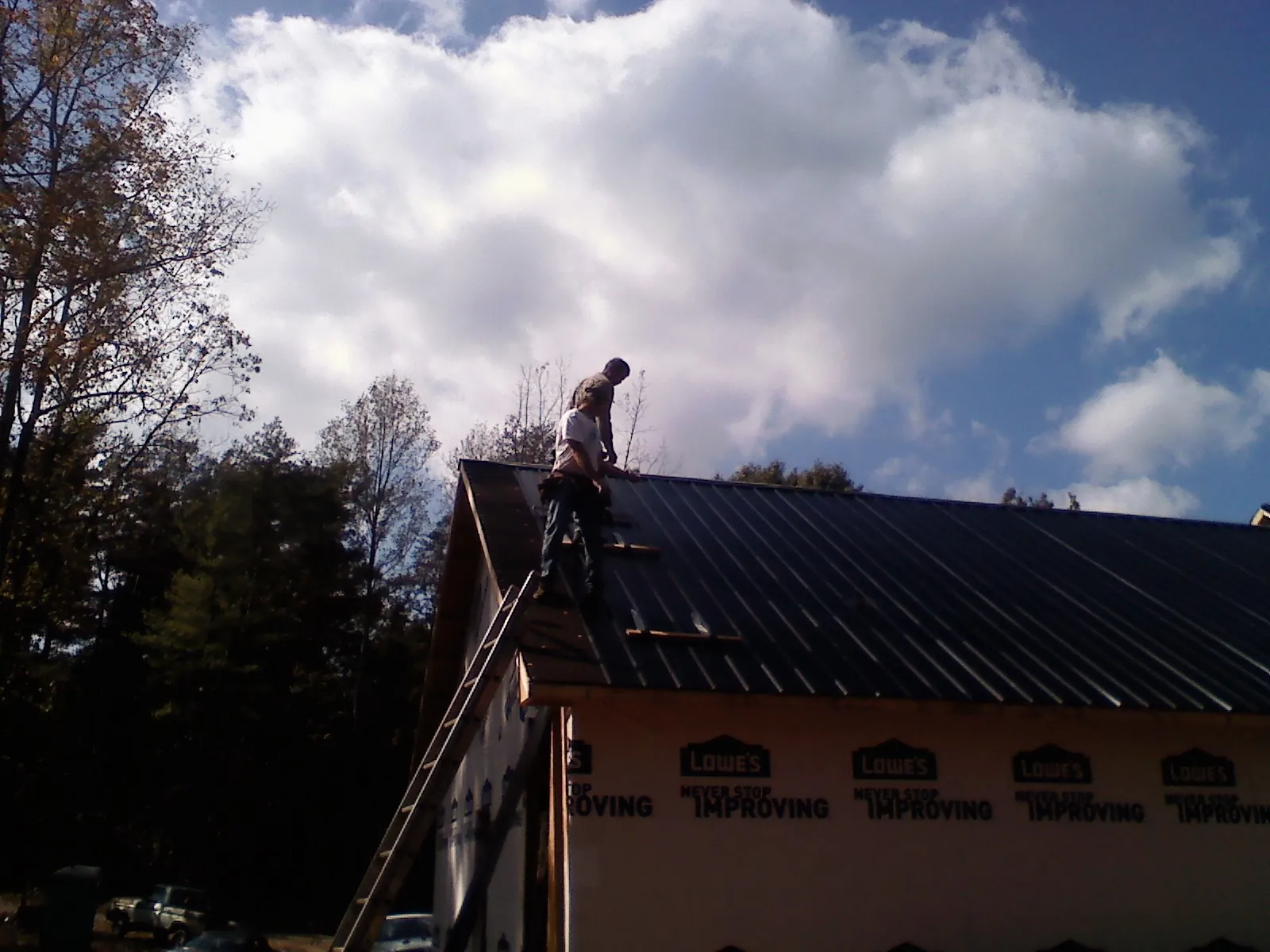 Roofer fastening dark metal panels high against a cloudy sky, from a Roof Inspection job in Nebo