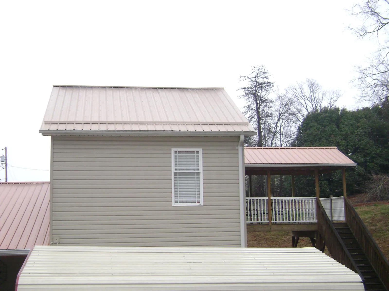 Tan metal roofs on a two story addition and attached porch, from a Roof Replacement job in Nebo